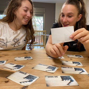 May include: Two people playing a game with cards featuring movie titles. The cards have a clapperboard design and the titles include "Die Hard", "Aladdin", "Casablanca", "La La Land", and "Moulin Rouge".