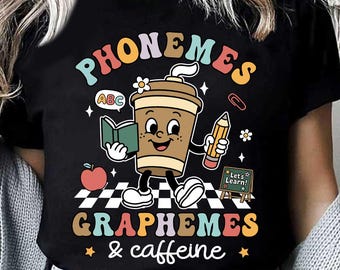 Könnte beinhalten: Schwarzes T-Shirt mit einer farbenfrohen Grafik, die eine Kaffeetasse-Figur mit einem Buch und einem Bleistift zeigt. Der Text lautet "PHONEMES, GRAPHEMES & caffeine" mit Illustrationen zum Thema Schule.