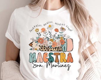 May include: White t-shirt with a colorful graphic of a pencil with flowers and the text "Enseñales, ámalos, miralos crecer MAESTRA Sra. Martinez".