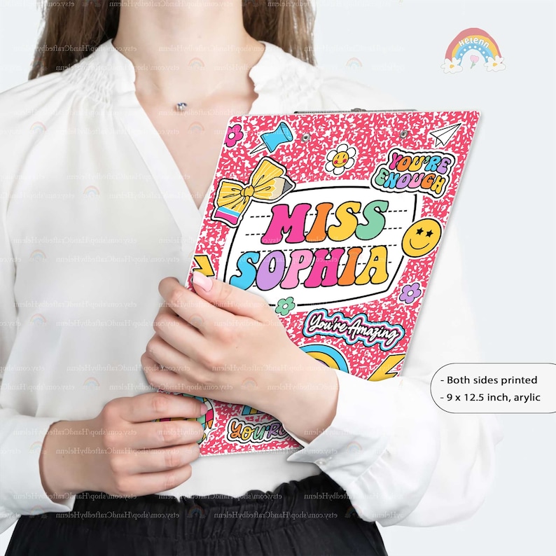 Puede incluir: Un portapapeles de acr&iacute;lico de 9 por 12.5 pulgadas con un fondo rosa moteado y pegatinas coloridas con el texto MISS SOPHIA, YOU'RE ENOUGH y YOU'RE AMAZING, junto con gr&aacute;ficos de un l&aacute;piz, una cara sonriente y un avi&oacute;n de papel.