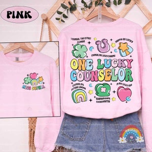 Puede incluir: Sudadera rosa con un dise&ntilde;o de arco&iacute;ris y tr&eacute;bol. El texto "One Lucky Counselor" est&aacute; en letras de arco&iacute;ris. El texto "Miss Sophia" est&aacute; en la parte delantera de la sudadera.