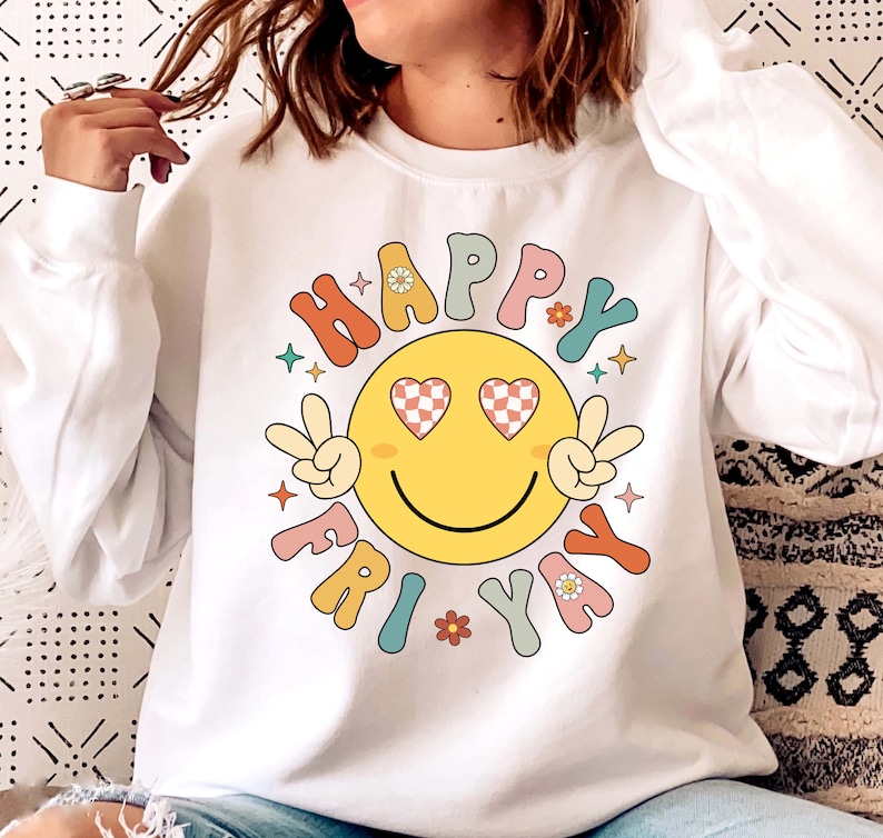 May include: White sweatshirt with a colorful graphic of a smiley face with heart-shaped eyes and the text "HAPPY FRIDAY" in a retro font.