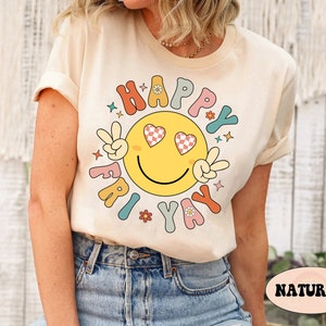 May include: A cream colored t-shirt with a retro smiley face graphic that says "Happy Fri-yay". The smiley face has checkered hearts for eyes and peace signs for hands.