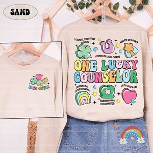 Puede incluir: Una sudadera beige con un dise&ntilde;o gr&aacute;fico colorido que dice "One Lucky Counselor". El dise&ntilde;o incluye arco&iacute;ris, corazones, estrellas, tr&eacute;boles y el texto "I counsel the cutest clovers", "Counseling lucky charms", "Counseling future leader", "Shenanigans coordinator", "In my lucky era" y "Happy go lucky".