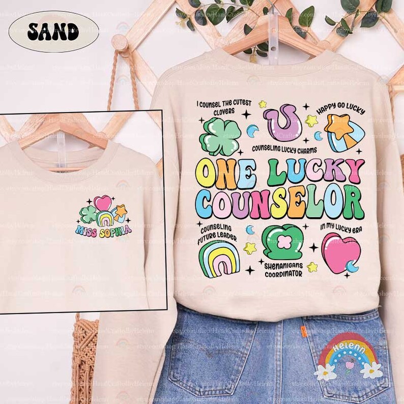 Puede incluir: Una sudadera beige con un dise&ntilde;o gr&aacute;fico colorido que dice "One Lucky Counselor". El dise&ntilde;o incluye arco&iacute;ris, corazones, estrellas, tr&eacute;boles y el texto "I counsel the cutest clovers", "Counseling lucky charms", "Counseling future leader", "Shenanigans coordinator", "In my lucky era" y "Happy go lucky".