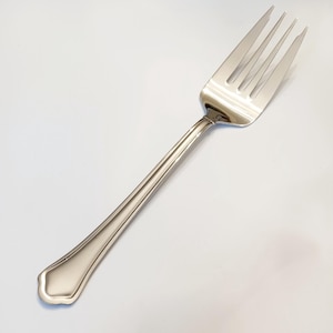 May include: A stainless steel fork with four tines. The handle has a decorative, ridged design and a rounded, scalloped end. The fork is designed for dining and is set against a white background.