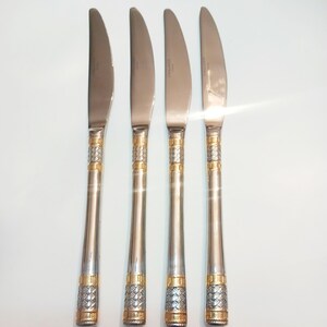 May include: Four silver and gold dinner knives with a decorative pattern on the handle.