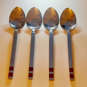 May include: Four silver spoons with red accents on the handles. The spoons have a rounded bowl and a long, straight handle.