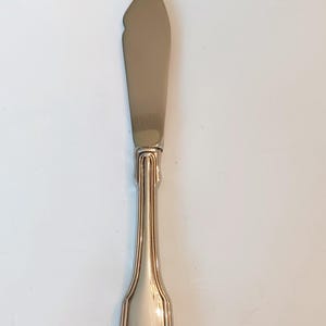 May include: A silver butter knife with a shell-shaped design on the handle.
