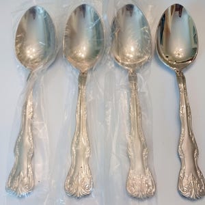 May include: Four silver spoons with ornate, detailed handles. The spoons are in clear plastic packaging, and the spoon bowls are oval-shaped. The handles have a floral and scroll design. The spoons are on a white surface.