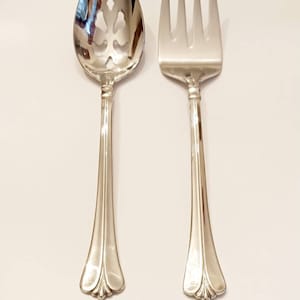 May include: A set of two silver serving utensils, a slotted spoon and a serving fork. Both utensils have a decorative, ornate handle.
