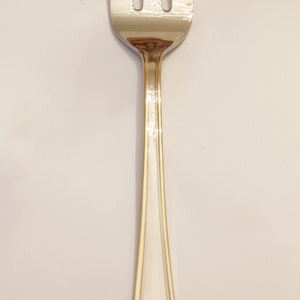 May include: A silver fork with a gold trim. The fork has a long, slender handle and four tines.