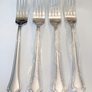 May include: Four stainless steel forks. One fork is separate, while the other three are in clear plastic packaging. The forks have a classic design with a decorative handle and four tines. The forks are on a white background.
