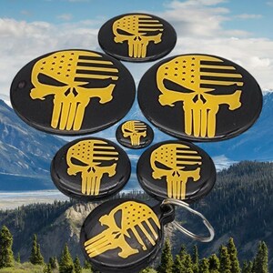 K&ouml;nnte beinhalten: Satz mit sechs runden schwarzen und goldenen Totenkopf-Schl&uuml;sselanh&auml;ngern mit amerikanischem Flaggen-Design. Die Schl&uuml;sselanh&auml;nger sind in Pyramidenform angeordnet, wobei der gr&ouml;&szlig;te Schl&uuml;sselanh&auml;nger oben und der kleinste unten ist.