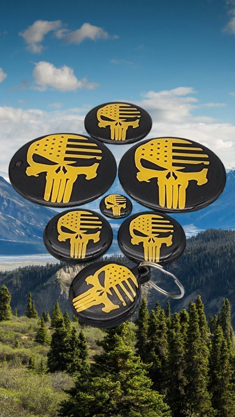 K&ouml;nnte beinhalten: Satz mit sechs runden schwarzen und goldenen Totenkopf-Schl&uuml;sselanh&auml;ngern mit amerikanischem Flaggen-Design. Die Schl&uuml;sselanh&auml;nger sind in Pyramidenform angeordnet, wobei der gr&ouml;&szlig;te Schl&uuml;sselanh&auml;nger oben und der kleinste unten ist.