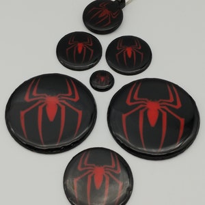 K&ouml;nnte beinhalten: Satz mit sechs runden Schl&uuml;sselanh&auml;ngern mit Spider-Man-Logo in Schwarz und Rot. Die Schl&uuml;sselanh&auml;nger haben eine gl&auml;nzende Oberfl&auml;che. Das Spider-Man-Logo ist rot und befindet sich mittig auf jedem Schl&uuml;sselanh&auml;nger. Die Schl&uuml;sselanh&auml;nger sind in verschiedenen Gr&ouml;&szlig;en.