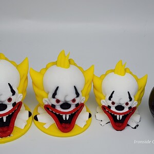 Op de afbeelding: Drie clownfiguren met witte gezichten, rode monden en geel haar. De clowns hebben rode ogen en staan op gele bases. Rechts van de clowns bevindt zich een zwarte bol. De tekst "Ironside Customs" staat in de rechterbenedenhoek.