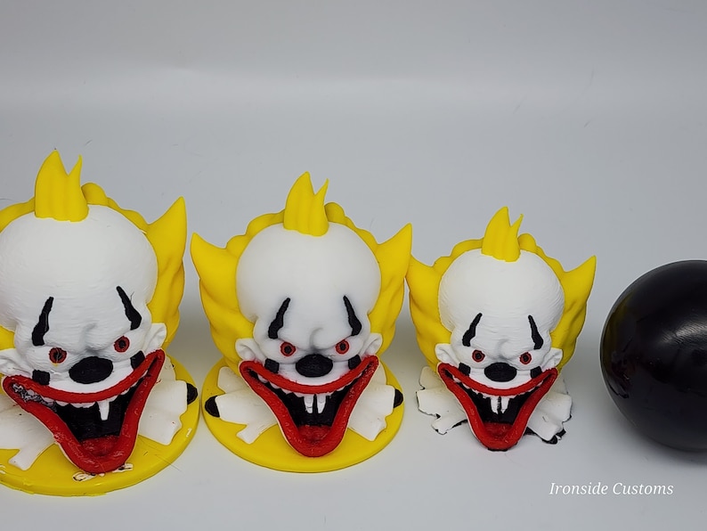 Op de afbeelding: Drie clownfiguren met witte gezichten, rode monden en geel haar. De clowns hebben rode ogen en staan op gele bases. Rechts van de clowns bevindt zich een zwarte bol. De tekst "Ironside Customs" staat in de rechterbenedenhoek.
