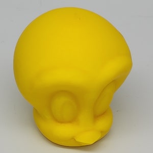 Op de afbeelding: Een felgele, driedimensionale figuur van het tekenfilmfiguur Tweety. De figuur heeft grote, ronde ogen, een kleine snavel en een afgerond hoofd. De figuur is gemaakt van een glad materiaal en staat tegen een effen achtergrond.