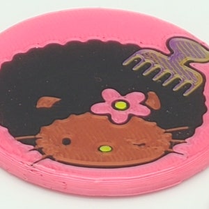 K&ouml;nnte beinhalten: Runder rosa Untersetzer mit einem schwarzen und braunen Hello Kitty-Charakter mit Afro-Frisur, einer rosa Blume und einem lila und goldenen Kamm.