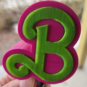 Op de afbeelding: Een 3D-geprinte koekjesvorm in de vorm van de letter "B". De groene letter staat in een roze omtrek. Het ontwerp heeft een afgerond lettertype en een dikke rand, ideaal voor bakken.