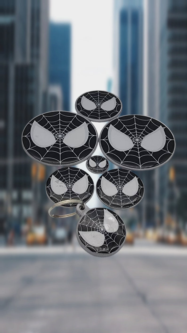 K&ouml;nnte beinhalten: Ein Set aus sechs schwarzen und wei&szlig;en Schl&uuml;sselanh&auml;ngern aus Metall mit einem Spider-Man-Design. Die Schl&uuml;sselanh&auml;nger sind rund und haben ein schwarzes Netzdesign mit einem wei&szlig;en Spider-Man-Gesicht in der Mitte. Die Schl&uuml;sselanh&auml;nger sind an einem silbernen Ring befestigt.
