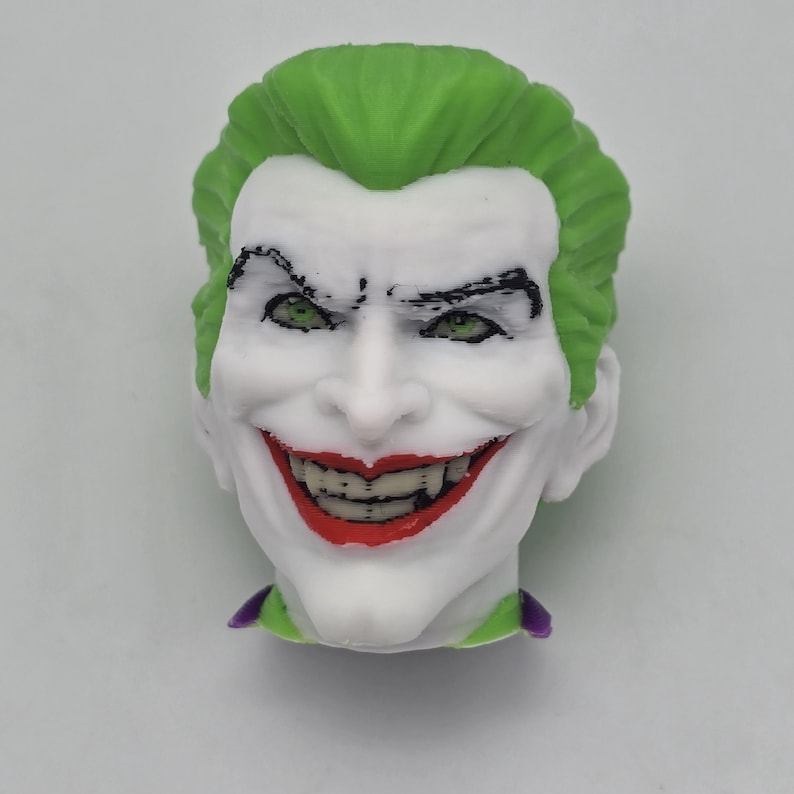 Op de afbeelding: 3D-geprinte buste van een personage met een witte huid, groen haar en een brede, roodgelipte grijns. Het personage heeft groene ogen, zwarte wenkbrauwen en een paarse kraag. De buste is een gedetailleerde weergave van een stripboekschurk.