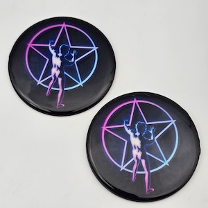 K&ouml;nnte beinhalten: Zwei schwarze runde Kn&ouml;pfe mit einem pinkfarbenen und blauen Pentagramm-Design. Eine Silhouette einer Person befindet sich im Pentagramm.