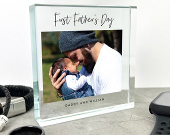 Puede incluir: Un bloque de foto de vidrio transparente con una imagen de un padre y su bebé. El texto "First Father's Day" está en la parte superior del bloque y el texto "Daddy and William" está en la parte inferior.