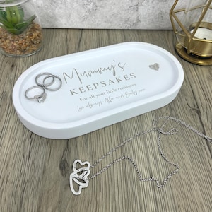 May include: White oval keepsake tray with the text "Mummy's Keepsakes" and a heart symbol. The tray holds three rings and a silver necklace with a heart pendant. The text "For all your little treasures" is also on the tray.