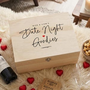 May include: A light-coloured wooden box inscribed with "Date Night Goodies" in cursive script. The box is personalised with "Nick & Liam's" above the text and a small red heart. The box is closed with a silver clasp.