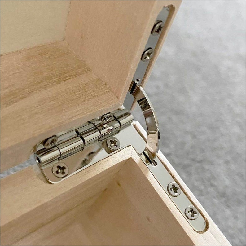 May include: Close-up of a wooden box with a partially open lid. The box is made of light-colored wood, and the hinges are shiny silver metal. The screws are also silver, contrasting with the wood.