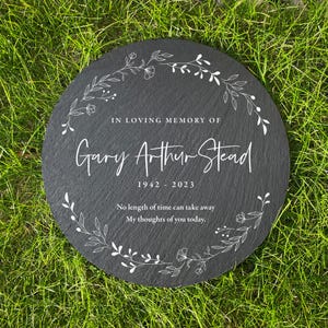 Könnte beinhalten: Eine schwarze Schiefer-Gedenktafel mit einem weißen floralen Kranzdesign. Die Tafel trägt die Inschrift "IN LOVING MEMORY OF Gary Arthur Stead 1942 - 2023 No length of time can take away My thoughts of you today."