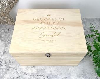 May include: A light-colored wooden keepsake box with a metal latch. The lid is engraved with the text MEMORIES OF MY HERO, a leaf design, the name Grandad, and the text LOVE YOU ALWAYS 1935 - 2025. The box has a smooth, natural wood grain finish.