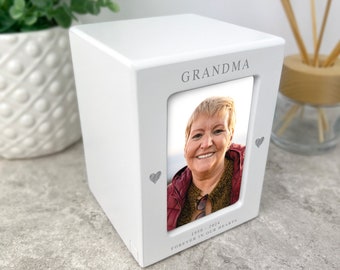 May include: White wooden box with a photo frame and the word "Grandma" printed on the front. The frame contains a photo of a woman smiling. The text "1930 - 2024 Forever in our hearts" is printed below the photo.