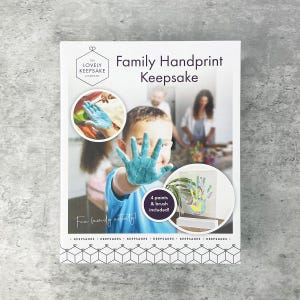 May include: A white Family Handprint Keepsake kit with the text "The Lovely Keepsake Company." The kit includes 4 paints and a brush. A child's hand is covered in blue paint, and the words "Fun family activity!" are written on the front.