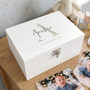 May include: A white wooden keepsake box with a silver clasp. The box is personalised with the name "Archie" in a script font, with the letter "A" in a light grey colour. The date and time of birth are also printed on the box.