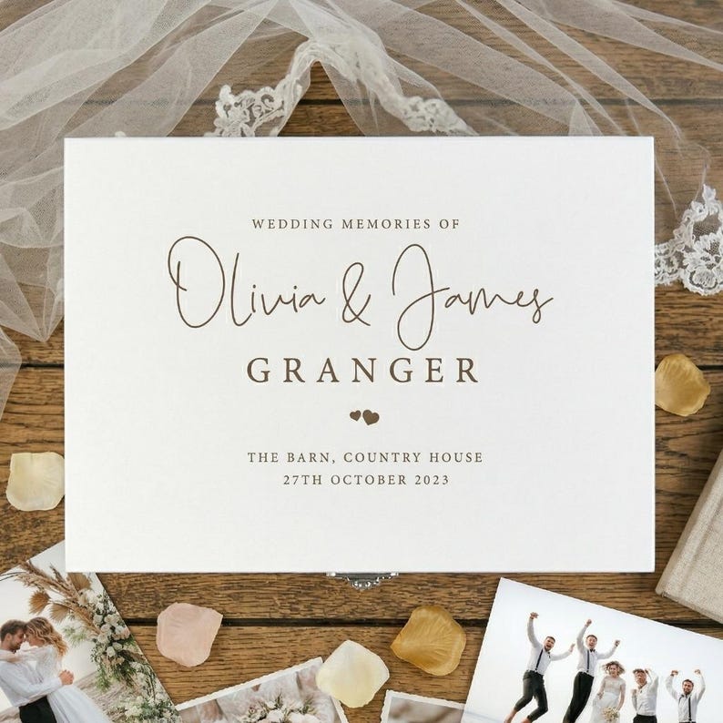 May include: A white wedding memory box with the text "WEDDING MEMORIES OF Olivia & James GRANGER" in brown script. The box also includes the date "27TH OCTOBER 2023". The box is surrounded by wedding photos and flower petals.