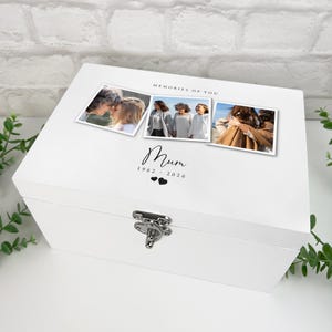 May include: A white wooden keepsake box with a silver clasp. The lid features three framed photos and the text "MEMORIES OF YOU" above the word "Mum" and the years 1962-2026, with two heart symbols below.