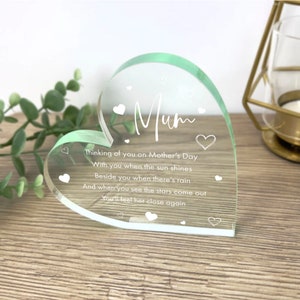 May include: A clear glass heart-shaped ornament with a green tint. The ornament has the word "Mum" engraved on it, along with a poem that reads: "Thinking of you on Mother's Day, With you when the sun shines, Beside you when there's rain, And when you see the stars come out, You'll feel her close again."