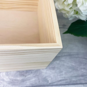May include: A rectangular wooden box with light beige natural wood grain patterns. The box features clean, straight edges and a smooth, unfinished surface. The interior base is flat and light-colored, showing the texture of the wood grain throughout.