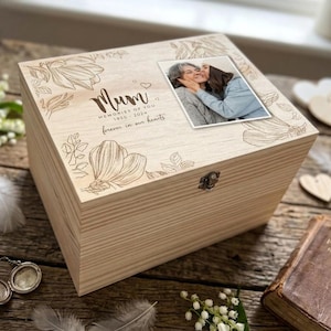 Peut inclure: Un coffret souvenir en bois clair avec une photo de deux personnes s'embrassant. La boîte est gravée de motifs floraux et du mot "Mum" ainsi que du texte "Memories of You 1950-2024 forever in our hearts."