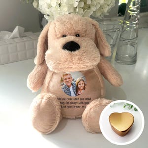Könnte beinhalten: Ein beigefarbener Plüschhund mit einem Foto eines Mannes und eines Mädchens in einem runden Rahmen auf seiner Brust. Der Rahmen trägt den Text "Told me close when you need hug. I'm always with you! Love you Forever xxx" darunter. Im unteren rechten Eck des Bildes befindet sich eine goldene herzförmige Erinnerungsbox.