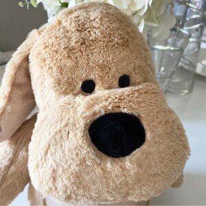 May include: A plush brown dog toy with black eyes and a black nose. The toy is made of soft, fluffy material.