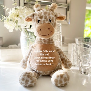 Puede incluir: Un juguete de peluche de jirafa con un diseño estampado en marrón y blanco. La jirafa tiene una cara sonriente y un mensaje personalizado que dice: "Bienvenido al mundo pequeño! William George Hunter 4 de octubre de 2023 Te queremos mucho xx"