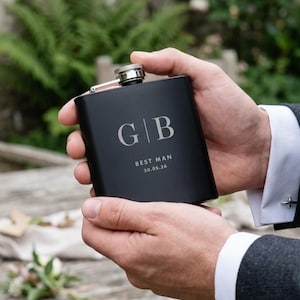 Könnte beinhalten: Eine schwarze Flasche mit den Initialen "G | B" und dem Text "BEST MAN 30.05.26" in heller Farbe. Die Flasche hat einen silbernen Verschluss und wird mit beiden Händen gehalten.
