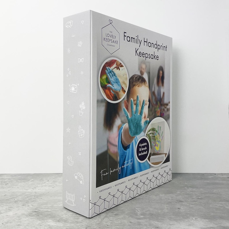May include: A white keepsake box with the text "Family Handprint Keepsake" and "The Lovely Keepsake Company." The box features images of a child with a blue handprint and a family. The box includes 4 paints and a brush.