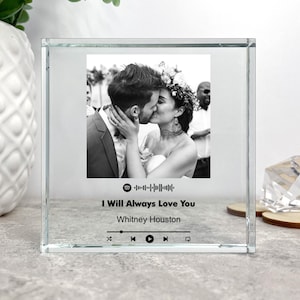 Op de afbeelding: Een helder glazen blok met een zwart-witfoto van een kussend stel. Het blok bevat het Spotify-logo, de songtitel "I Will Always Love You" van Whitney Houston en afspeelknoppen. Een decoratief aandenken met een bruiloftthema.