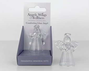 May include: Clear glass angel figurine with detailed wings and a halo. The angel is displayed next to its packaging, which reads "Angels, Wings & Feathers" and "Comforting Glass Angel". The packaging is a light purple color.