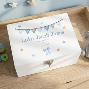 May include: A white wooden keepsake box with a silver clasp. The lid is decorated with blue and grey pennant flags, the name "Luke Jacob Jones", birth details, and star and bow illustrations. The box is a baby-themed gift.